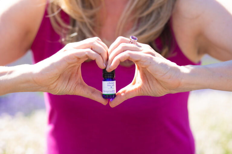 A person holding a small bottle of lavender essential oil with their hands forming a heart shape around it.